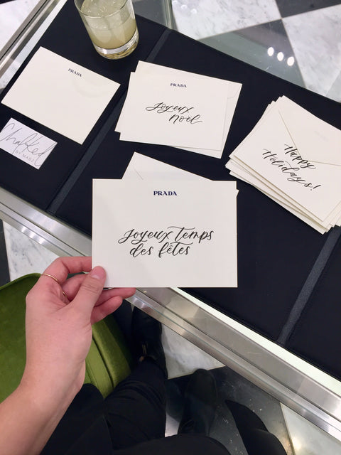 Many hand written Prada embossed note cards display holiday greetings in both french and english. Each card is white with elegant black modern calligraphy.