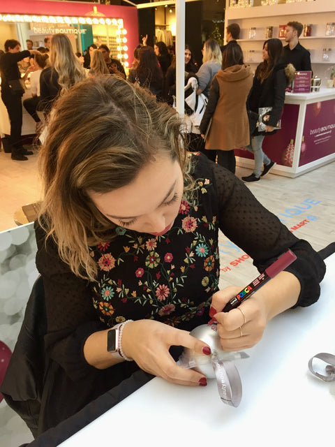 Modern calligrapher Chalked by Mabz hand letters a silver Christmas ornament live at an event for Shoppers Drug Mart Beauty Boutique