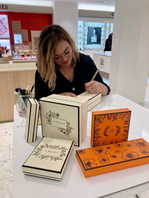 Live event calligrapher and floral illustration artist Chalked by Mabz works on customizing gift boxes for Jo Malone and Prada at Holt Renfrew Ogilvy in Montreal