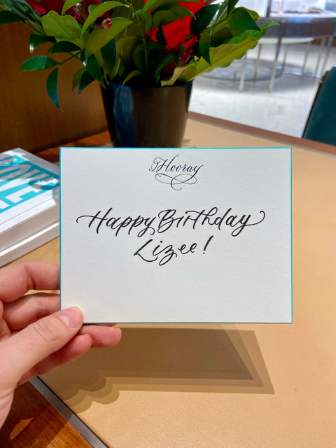 "Happy Birthday Lizee!" is written in modern calligraphy on a notecard with Tiffany blue edges