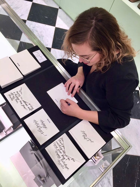 Mabz, a modern calligrapher, sits behind the counter at Prada in Montreal as she does calligraphy on custom holiday greeting cards
